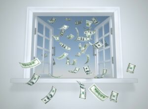 Dollar bills fly out of a window, representing wasted money.