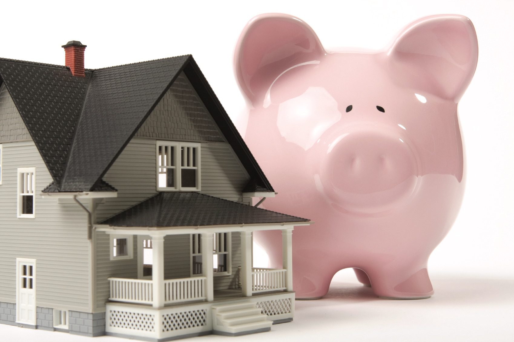 Gray house next to large pink piggy bank; saving for home concept.