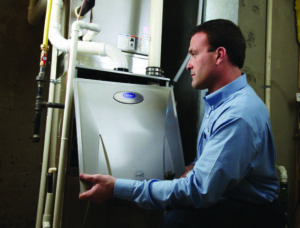 Man in blue shirt inspecting furnace by opening access panel.