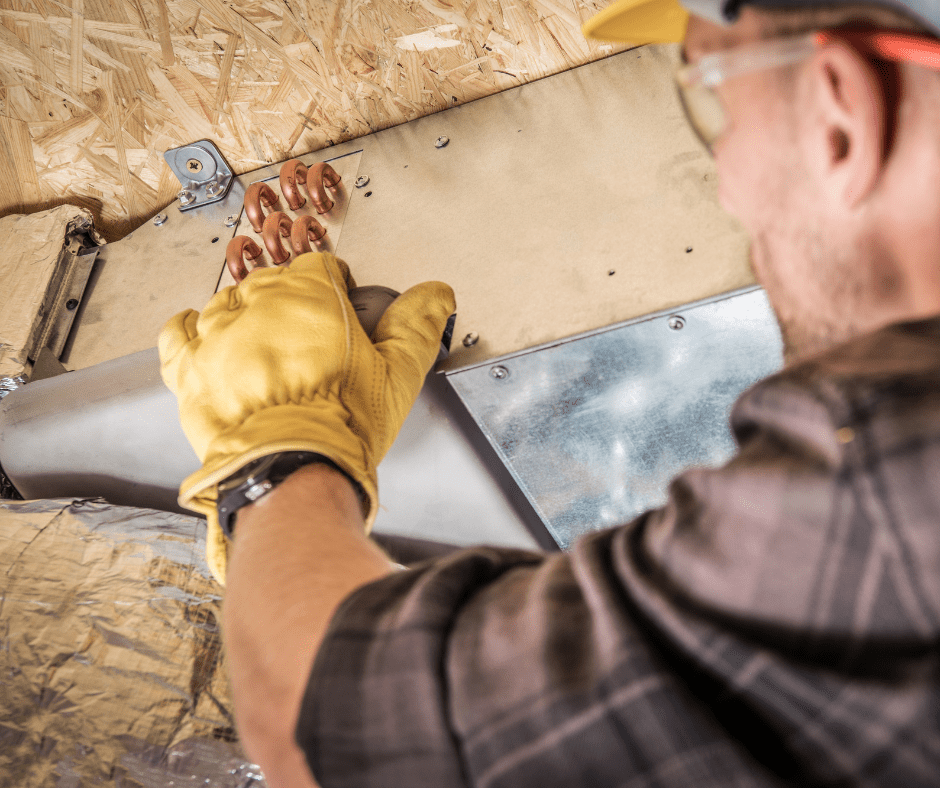 Worker installs copper tubes on AC, wearing gloves, glasses, and hat.