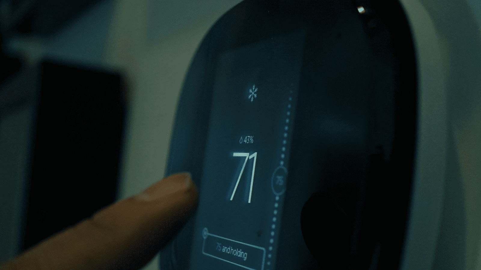 A finger adjusts a digital thermostat set to 71, holding at 75.