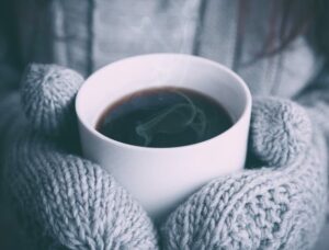 warm cup of coffee with gray mittens