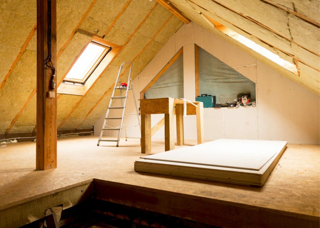 Under-construction attic with ladder, work table, insulation, and plywood.